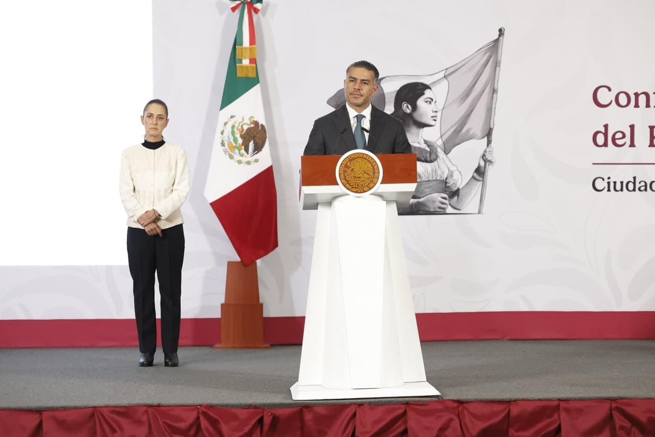Omar García Harfuch, secretario de Seguridad, ofrece un discurso en un evento en Ciudad de México, con bandera de México de fondo.