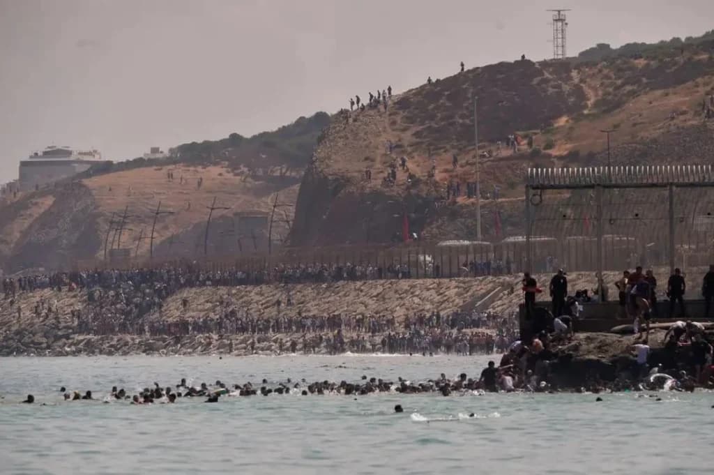 Migrantes intentando cruzar a Ceuta desde Marruecos, con una multitud en la frontera y en el agua, reflejando la crisis migratoria.