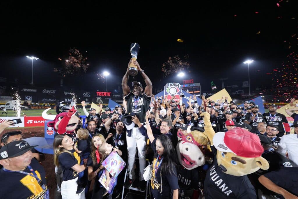 Jugadores de los Toros de Tijuana celebran con el trofeo de campeones de la LMB, rodeados de aficionados y fuegos