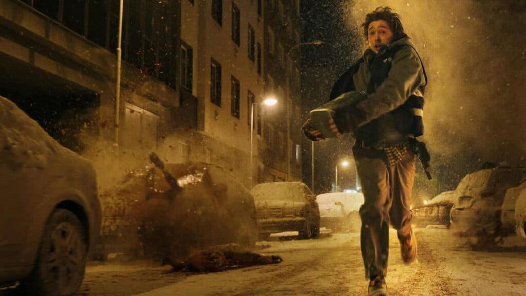 Un personaje corre por una calle nevada, sosteniendo un objeto, mientras explotan vehículos en el fondo, reflejando la tensión de Resident Evil.