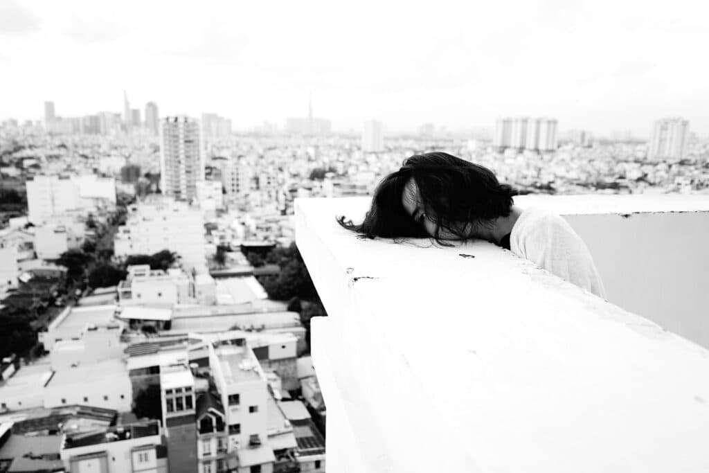 Persona con cabello oscuro apoyada en un borde de un edificio alto, con una vista panorámica de la ciudad al fondo,